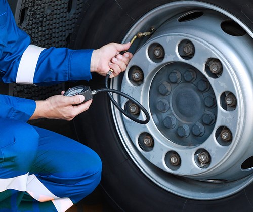 Technician in blue jumpsuit using tool to check tire pressure